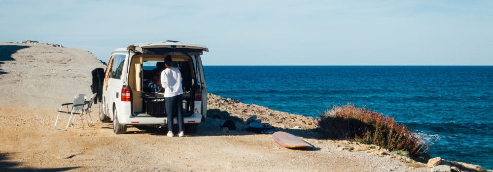 A camper van parked by the sea, with its trunk open.